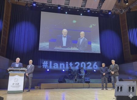 Dos ponentes en el escenario de la 31ª Noche de las Telecomunicaciones y la Informática IANIT 2026 con pantalla de proyección al fondo